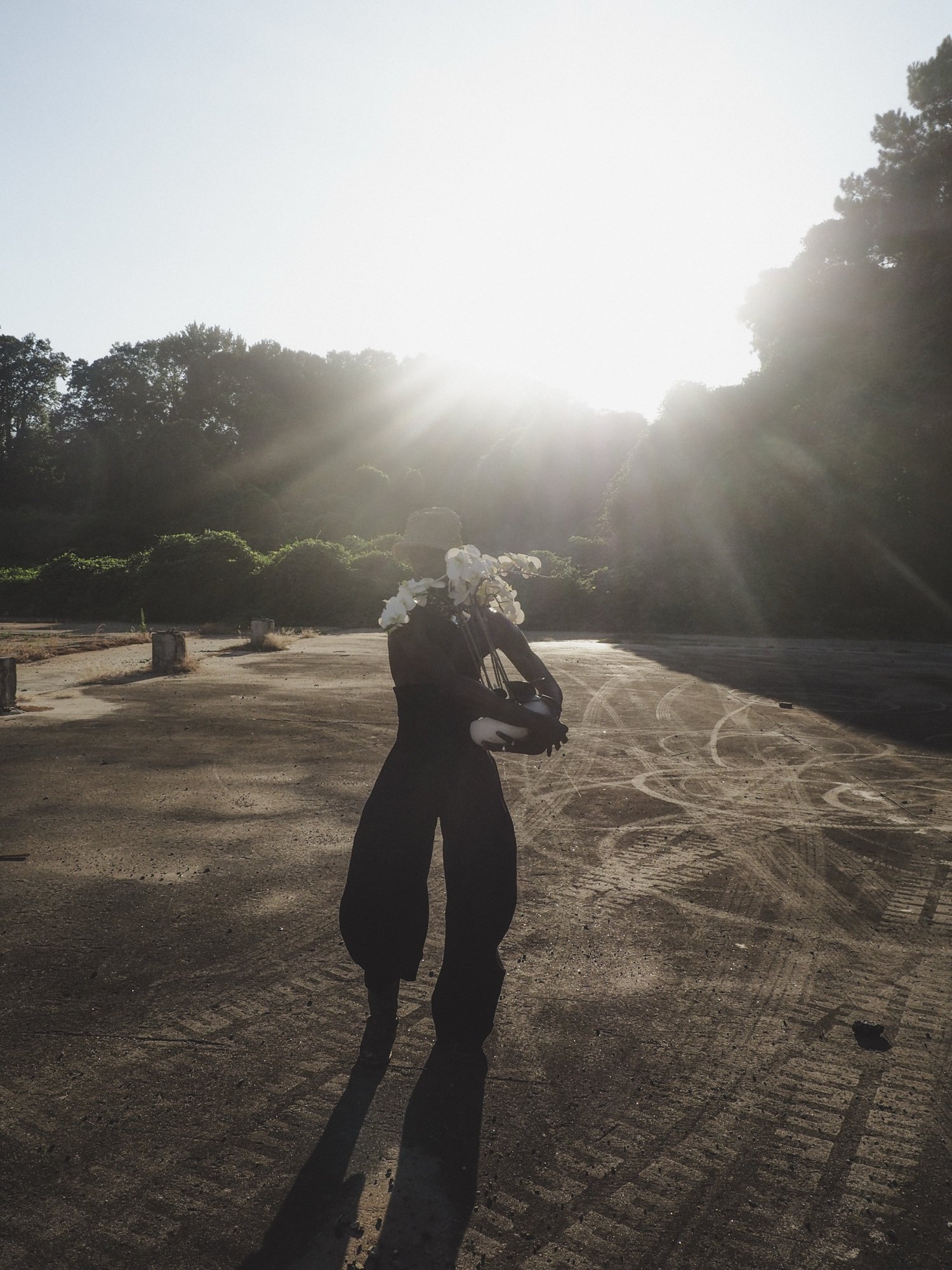 W.J. Lofton in silhouette against a low sun, holding orchids, his shadow stretching across the pavement.